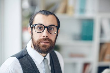 Ofiste çalışan, gözlüklü, korkmuş, zeki, sakallı genç girişimcinin portresi.