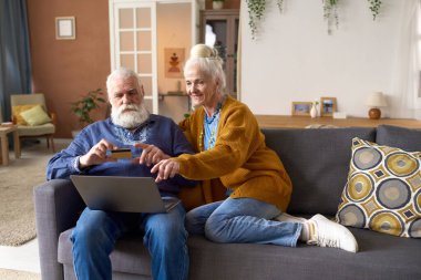 Üst düzey çift kanepede dizüstü bilgisayarlarıyla oturuyor ve online kredi kartıyla ödeme yapıyorlar.