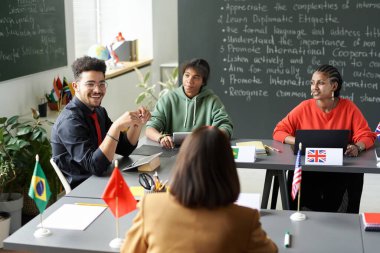 Rear view of teacher talking to multiethnic students during seminar in the classroom clipart