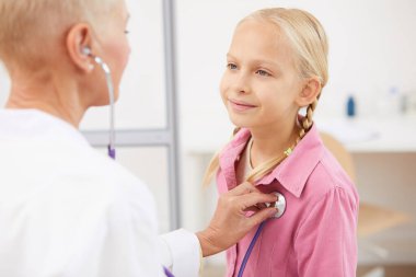 Klinikte steteskoplu genç bir hastayı muayene ederken ciğerlerini dinleyen kadın doktor.