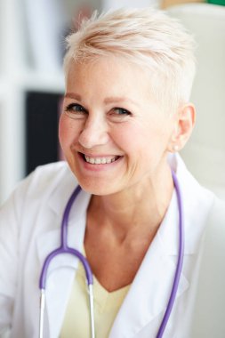 Ofiste boynuna steteskop takan mutlu, olgun, sarışın bir kadın doktorun portresi.