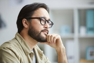Ofiste çalışırken derin düşüncelere dalan ciddi yaratıcı Asyalı genç adamın yakın çekimi.