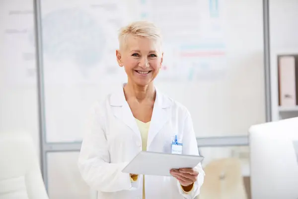 Portrait of cheerful beautiful female neurologist in lab coat using digital tablet at medical conference