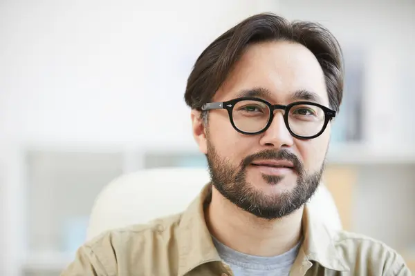 Close-up of content intelligent young Asian man with beard wearing eyeglasses working in office