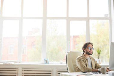 Ciddi hipster genç Asyalı sakallı uygulama geliştiricisi masada oturuyor ve yeni uygulamayı test ederken bilgisayar kullanıyor.