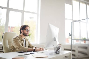 İçerik hipster genç Asyalı tasarımcı gündelik gömlekli masada oturuyor ve arayüz tasarımı oluştururken klavyeye yazı yazıyor