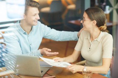 Keyifli genç pazarlamacılar rahat bir kafede oturmuş veri raporuyla çalışırken gülüyorlar.