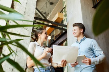 Çağdaş lobide duran ve çizimler üzerinde çalışırken birbirlerine bakan pozitif genç tasarımcıların bakış açısının altında