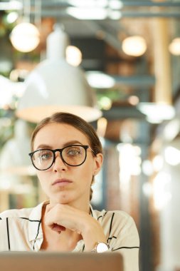 Cafe 'de modern dizüstü bilgisayar kullanarak kendine güvenen, şık gözlüklü çekici genç bir kadının portresi.