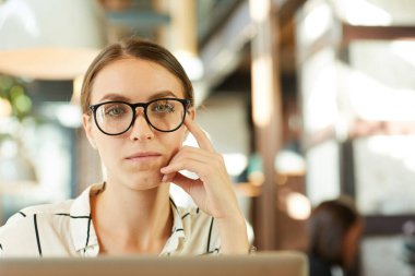 İçerik portresi, gözlüklü zeki bayan girişimci lobideki masada oturuyor ve dizüstü bilgisayar kullanıyor.
