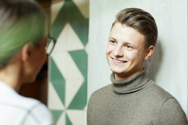 Kadınlar modern lobide dikilirken balıkçı yakalı genç bir adamla konuşuyor.