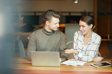 Birlikte çalışma alanında masada oturan ve iş sunumunda birlikte çalışırken dizüstü bilgisayar kullanan pozitif genç analistler