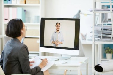 Resmi ceketli düşünceli genç iş kadını masada oturmuş, internetten iş kursuna çalışırken monitöre bakıyor.