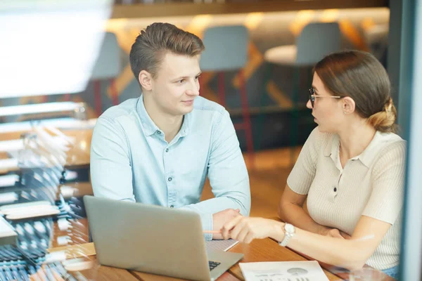 Shocked young businesswoman pointing at laptop screen while offering development strategy to colleague at meeting in cafe