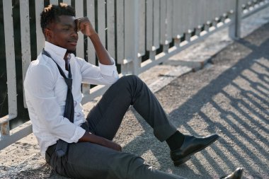 Depresyondaki Afrikalı Amerikalı adam köprüde oturmuş sorunlarını düşünüyor.