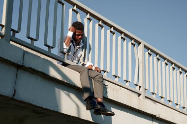 Bilekleri bandajlı Afrika kökenli Amerikalı bir adam köprüde oturup intihar etmeyi düşünüyor.