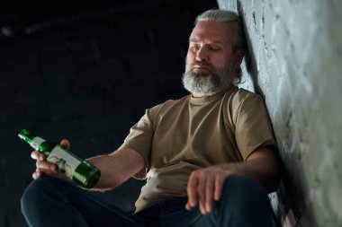 Olgun sakallı adam alkolle sorun yaşıyor, yerde alkol şişesiyle yatıyor.