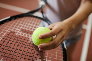 Tanımlanamayan bir kadının tenis topunu rakete koyup maçtan önce servis yapma çabasının yakın çekimi.