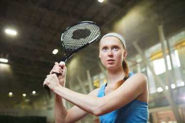 Geniş kortta duran ve topa vurmak için tenis raketini kavrayan kırmızı örgülü genç bir kadın.