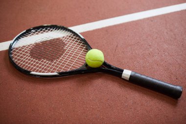 Tenis raketinin ve tenis kortunun kırmızı zeminine yerleştirilmiş yeşil topun yakın çekimi.