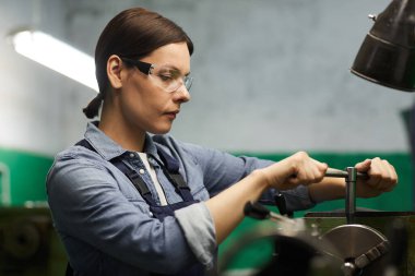 Odaklanmış orta yaşlı kadın manuel torna operatörü makineyi işe hazırlarken metal kolu büküyor