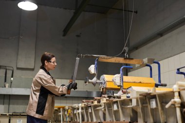 Koruyucu iş kıyafetleri içinde ciddi esmer kadın taşıyıcı ve montaj hattında kontrol paneli ile çalışıyor