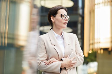 Kasıtlı olarak orta yaşlı, şık ceketli çekici bir iş kadını lobide durmuş, akıllı telefon tutuyor ve meslektaşını bekliyor.