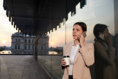 Ciddi derecede düşünceli esmer kadın çağdaş binanın yanında duruyor ve projeyi tartışmak için meslektaşını telefonla arıyor.