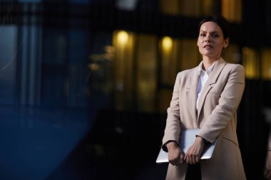 Bilgisayarı tutan ve büyük şehirde yaşayan orta yaşlı iş kadınının kasıtlı portresi.