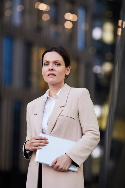 Portrait of content successful female business expert in elegant jacket holding portable gadget outdoors