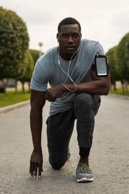 Koşucu başlamaya hazırlanıyor. Genç kaslı zenci bir sporcunun portresi. Kulaklıkları dizinde duruyor ve kameraya bakıyor.