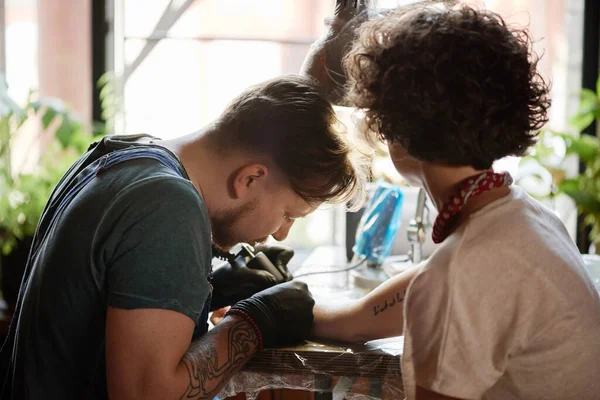 Professional male tattooist drawing a tattoo on hand of female client with electric tattoo gun