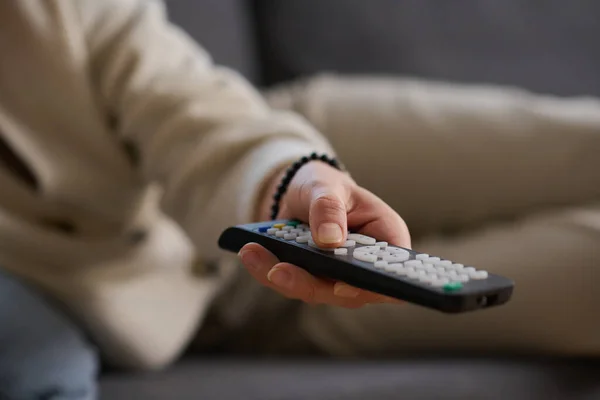 Close-up of woman using remote control to watch TV while lying on sofa in the room