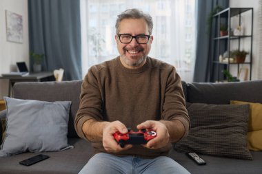 Odadaki kanepede video oyunu oynamak için joystick 'in düğmelerine basan mutlu adamın portresi