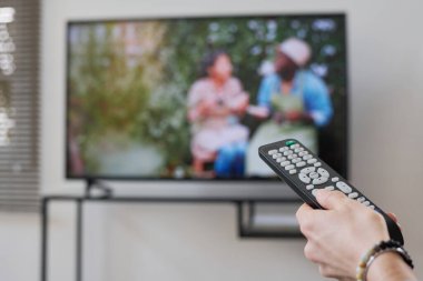 Evde dinlenirken televizyonu açmak için uzaktan kumanda kullanan kadının yakın plan görüntüsü