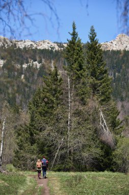 Sırt çantalı genç çift uzaktaki ağaçlık ve kayalık dağlara doğru yürüyorlar.