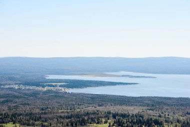 Uçsuz bucaksız vahşi orman ve yanında küçük bir yerleşim yeri bulunan büyük göl manzarası. Urallar, Rusya