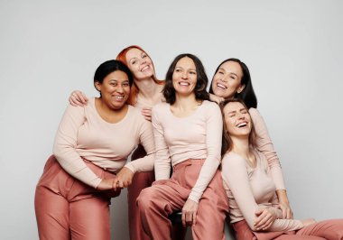 Farklı etnik kökenlere sahip mutlu kadınlar beyaz arka planda birlikte gülüyorlar.