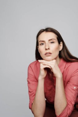 Düşünceli, kahverengi saçlı bir kadının portresi. Dudakları hassas. Başı beyaz arka plana yaslanmış.