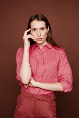 Çekici genç bir kadının portresi kahverengi arka planda tapınağa dokunan düşünceler üzerine odaklanmış.