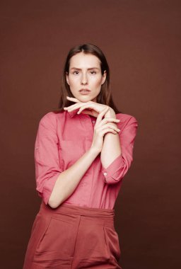 Çekici, uzun saçlı genç bir bayanın portresi yalnız kahverengi arka planda poz verirken el üstünde duruyor.