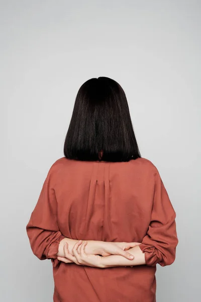 Rear view of unrecognizable brunette woman with tired hands behind back against isolated background