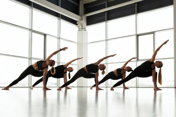 Group of young women in black sportswear stretching body while practicing yoga in studio
