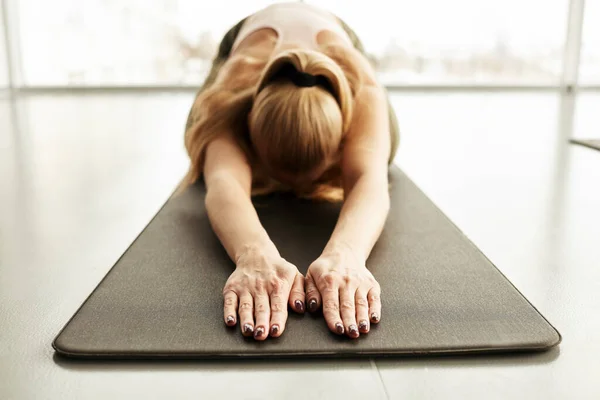Young woman lying in childs pose on yoga mat while training in health club