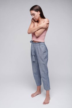 Korkmuş genç esmer kadın sevilmediğini hissediyor gözlerini kapalı tutuyor ve gri arka plana sarılıyor.