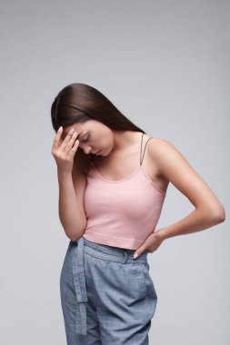 Ciddi genç esmer kadın, günlük kıyafetiyle, migrenden muzdaripken alnını ovuyor, izole bir geçmişi var.