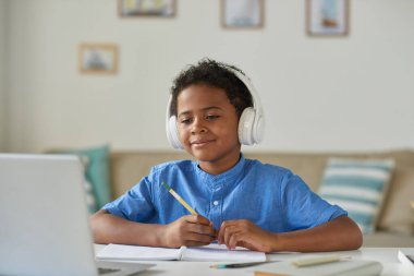 Kablosuz kulaklıklı meraklı Afro-Amerikalı çocuk video konferans uygulaması üzerinden öğretmenle konuşurken dizüstü bilgisayar kullanıyor.