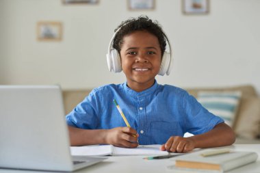 Mavi tişörtlü, gülümseyen zenci çocuğun portresi evde oturmuş çalışma kitabına not alıyor.