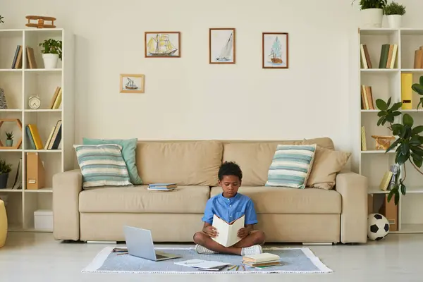 Soustředěný Černý Chlapec Zkříženýma Nohama Podlaze Čtení Učebnice Při Přípravě — Stock fotografie