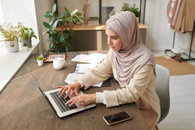 Orta Doğulu iş kadını şık başörtüsü takıyor ve abaya modern iş yerinde dizüstü bilgisayarda çalışıyor, yüksek açılı çekim